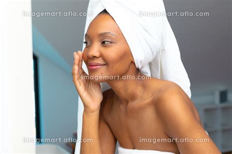 Young African American Woman With Head Wrapped In White Towel Touching Her Cheek In Bathroom