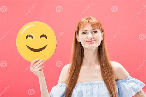 View Of Cheerful Redhead Girl Holding Smiley Isolated On Pink Stock