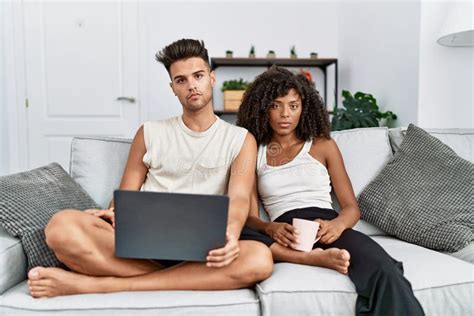 Young Interracial Couple Using Laptop At Home Sitting On The Sofa