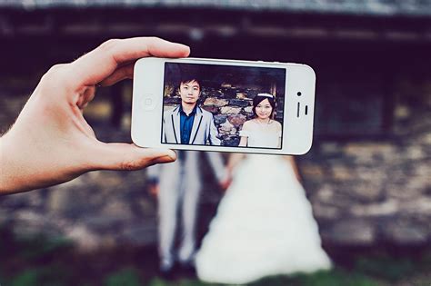 A Person Holding Up A Cell Phone To Take A Photo With The Bride And Groom