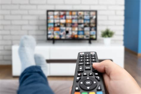Man Laying On Sofa Binge Watching Tv With Remote Control In His Hand