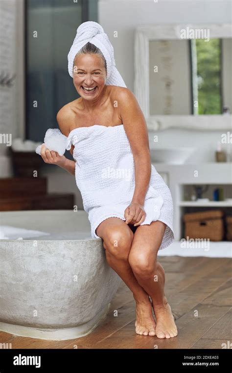 Happy Mature Woman Playing With Bubbles While Sitting At Edge Of Bathtub In Bathroom Stock Photo