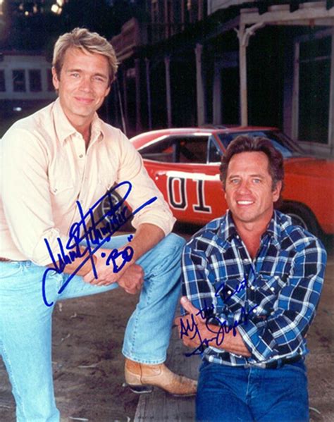 Two Men Sitting On The Ground In Front Of A Red Car With Autographs