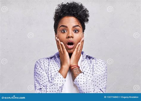 Impressed Amazed Woman With Afro Hair Drops Jaw Keeps Both Hands On Cheeks Dressed In Casual T