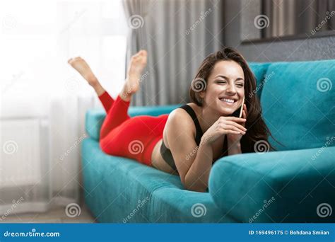 Fit Brunette Woman In Red Sport Leggings And Black Top Lying On Sofa Having Pleasant