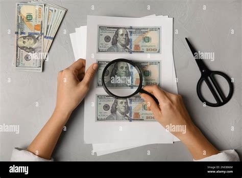 Counterfeiter examining sheet of paper with dollar banknotes at grey