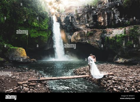 Couple In Love Kiss Against The Backdrop Of A Picturesque Waterfall Hidden In The Tropical Rain