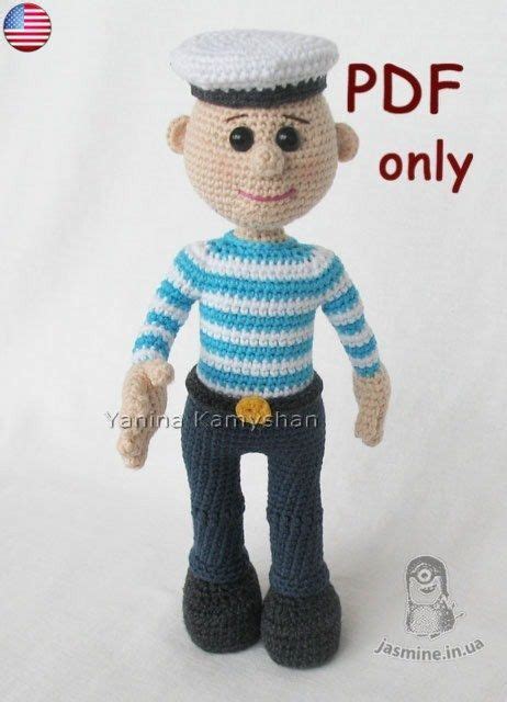 A Crocheted Doll With A Sailors Hat And Blue Pants Is Posed On A White