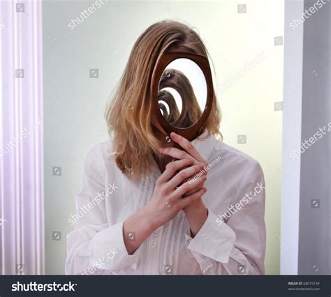 a girl holding a mirror over her face in front of a larger mirror creating the illusion of