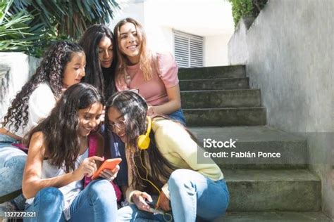Group Of Happy Latina Teen Girls In A Bleacher Using Their Cell Phones Or Smartphones To View