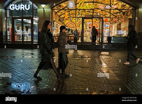 Two Women Walking In Arbat Street At Night Pass By The Brightly