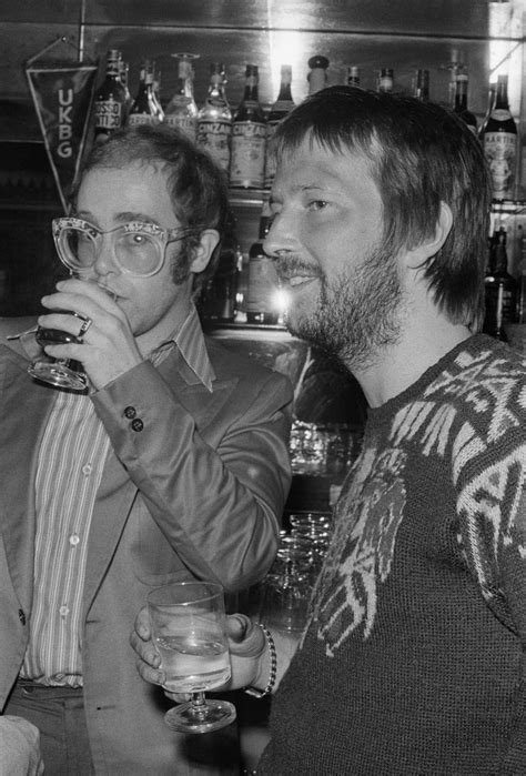 Two Men Standing Next To Each Other At A Bar With Drinks In Front Of Them