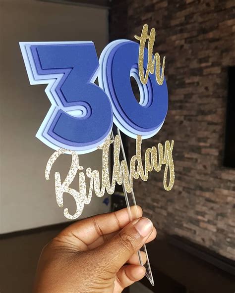 Someone Holding Up A Blue And Gold 30th Birthday Cake Topper