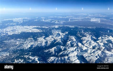 An Aerial View From An Airplane Window Of Mountains Snow Clouds And
