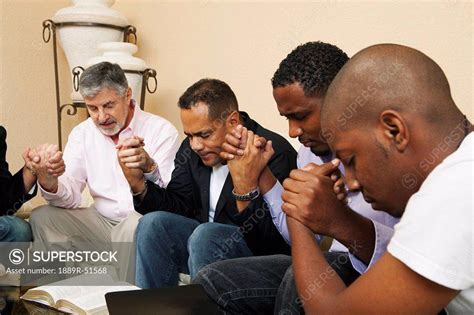 A Group Of Men Praying Together With An Open Bible Superstock
