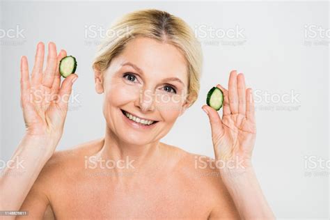 Beautiful And Smiling Mature Woman Holding Cut Cucumber And Looking At
