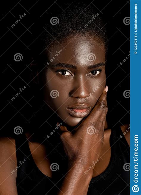 portrait of beautiful african american woman holding hand on chin and looking at camera stock