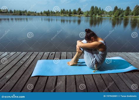 A Young Woman On A Wooden Dock Sits On A Blue Mat In A Fetal Position