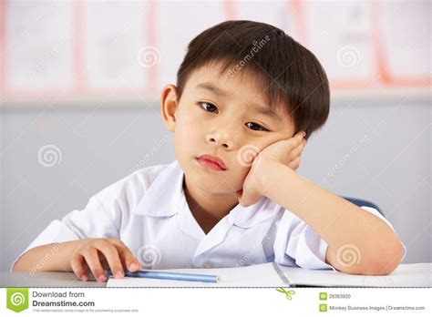 Unhappy Male Student Working At Desk In School Stock Photo