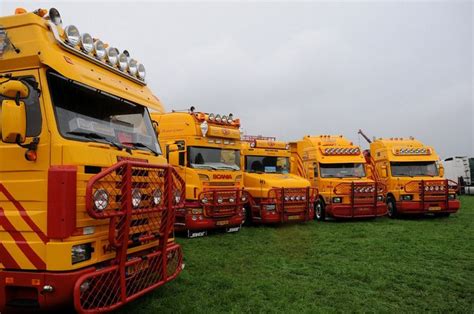 A Row Of Yellow Trucks Parked Next To Each Other On Top Of A Lush Green