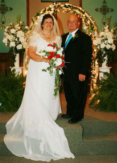 A Man And Woman Standing Next To Each Other In Front Of A Wedding Arch
