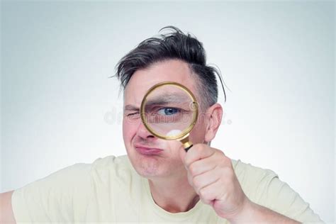 Funny Young Man Looking Through Magnifying Glass On Light Background
