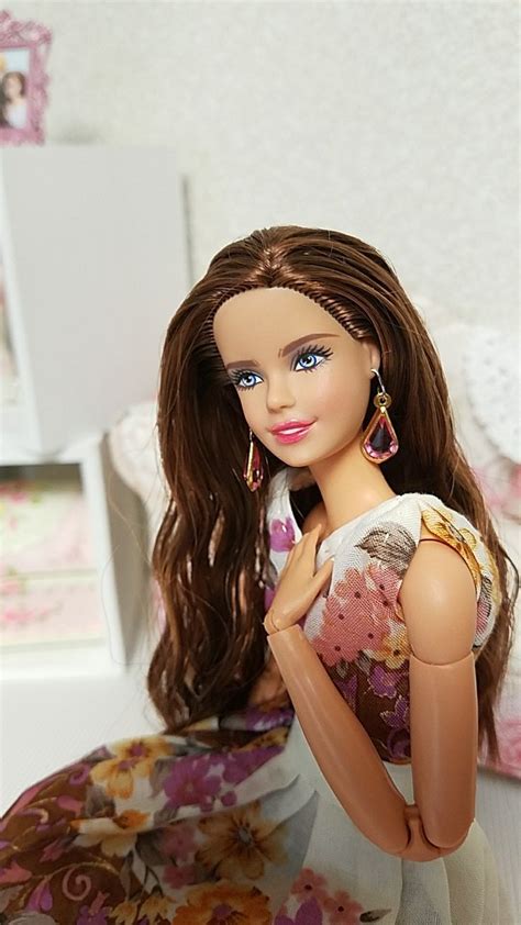 A Doll With Long Brown Hair And Blue Eyes Sitting On Top Of A Bed In A