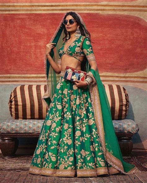 A Woman In A Green And Gold Lehenga Standing Next To A Couch With Her