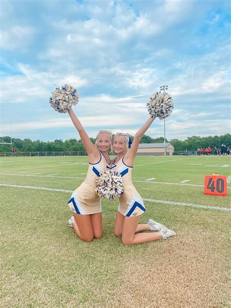 Two Cheerleaders Kneeling On The Ground With Their Hands In The Air