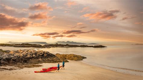 Couple Pulling Red Canoes Across Sandy Beach In Scotland At Sunset