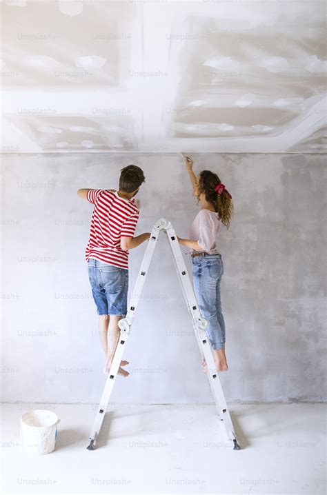 Beautiful Young Couple Standing On Ladder Painting Walls In Their New