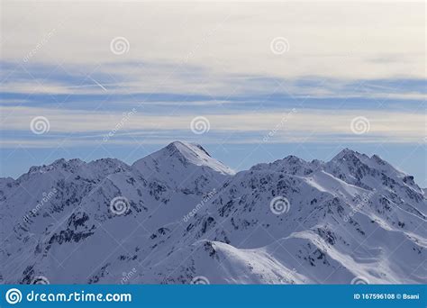 Snowy Slope In High Winter Mountains And Sunlit Cloudy Sky At Evening