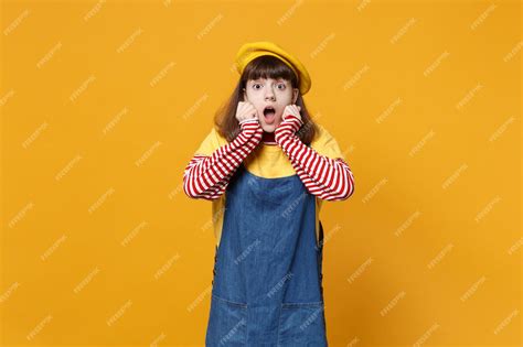 Шокированная девочка подросток во французском берете джинсовом сарафане с широко открытым ртом