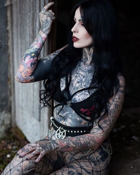 A Woman With Black Hair And Tattoos On Her Body Sitting In Front Of A Door