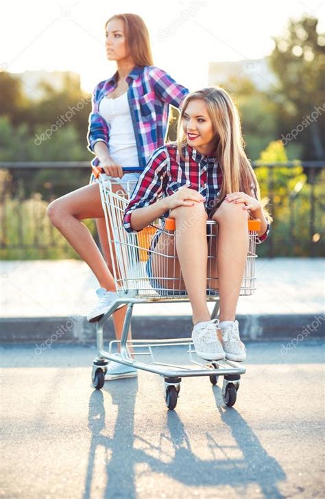 Two Happy Beautiful Teen Girls Driving Shopping Cart Outdoors Stock