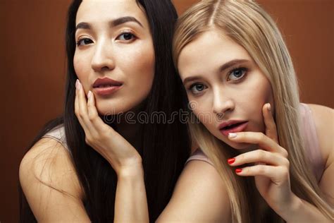 Two Pretty Diverse Girls Happy Posing Together Blond And Brunette Caucasian And Asian On Brown