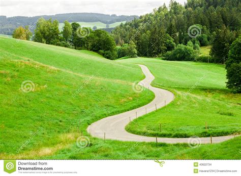 Winding Country Road Between Green Fields In The Mountains Stock Photo