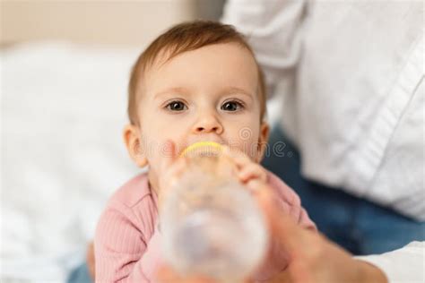 Cute Infant Baby Girl Drinking Water From Bottle Sitting On Bed With