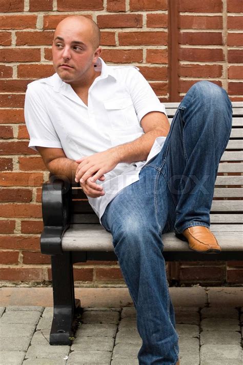 A Man In His Twenties Sitting Casually On A Bench In An Urban Area