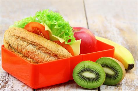Healthy School Lunch Box Containing Whole Grain Cheese Roll Apple Banana And Kiwi Fruit Stock