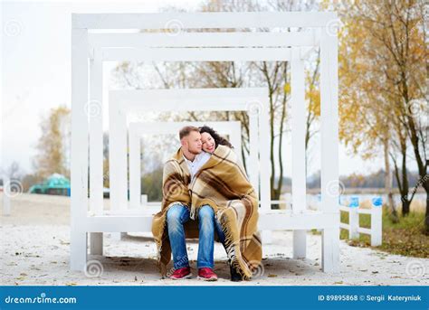 Young Couple Embracing And Covered With A Warm Blanket Sitting O Stock