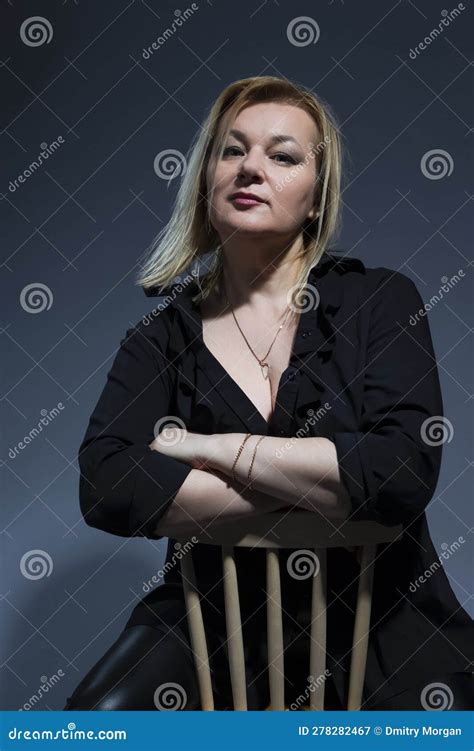 sensual mature confident caucasian woman in black shirt sitting on chair on dark background